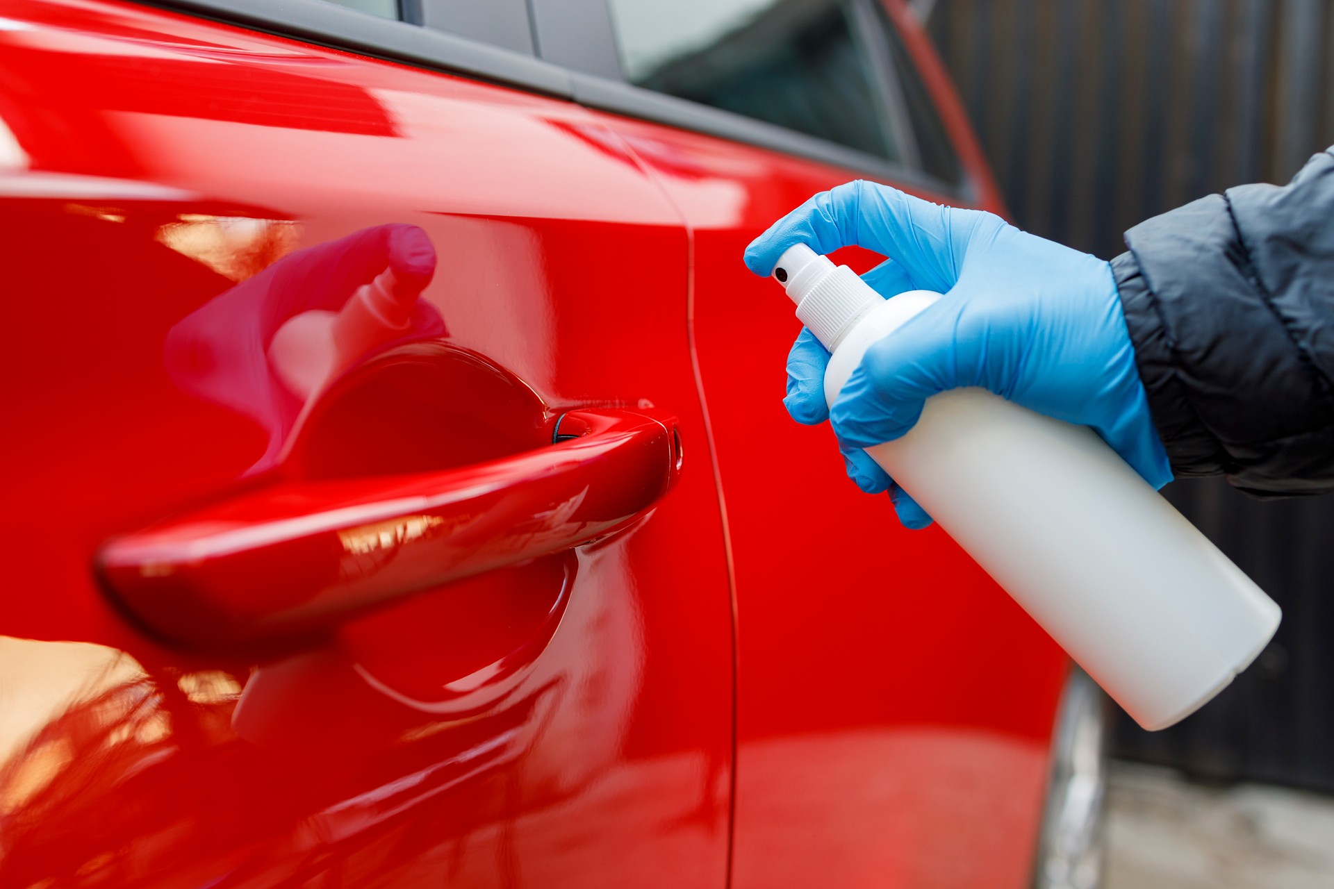 Person wearing gloves and spraying car with disinfectant